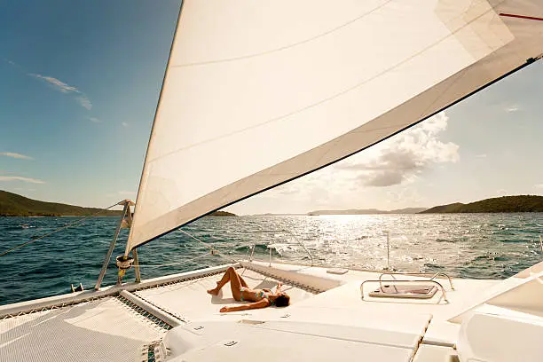 woman in bikini sunbathing on a catamaran and enjoying sailing through the Caribbean
