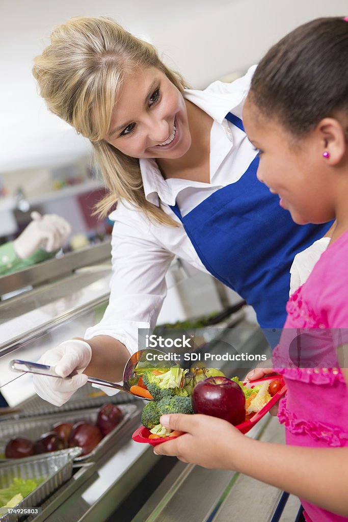 Lady aiutando bambina con cibo a pranzo linea - Foto stock royalty-free di Edificio scolastico