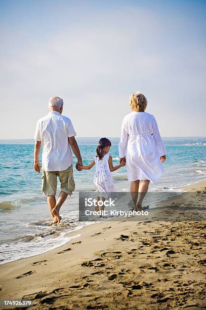 Niña Y Su Abuelos Caminatas En La Playa Foto de stock y más banco de imágenes de Niño - Niño, Playa, Litoral