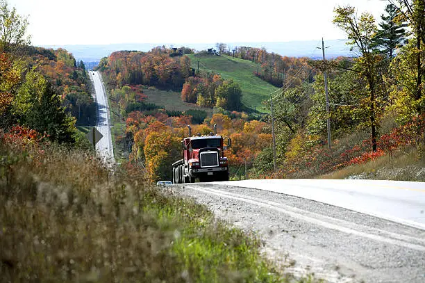 truck coming over the brow of a steep hill in a rural location fulled with autumn colour