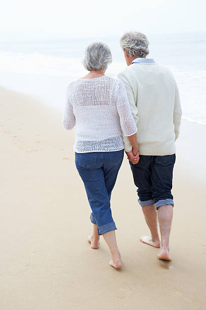 istock Senior couple holding hands and walking along a beach 174927590