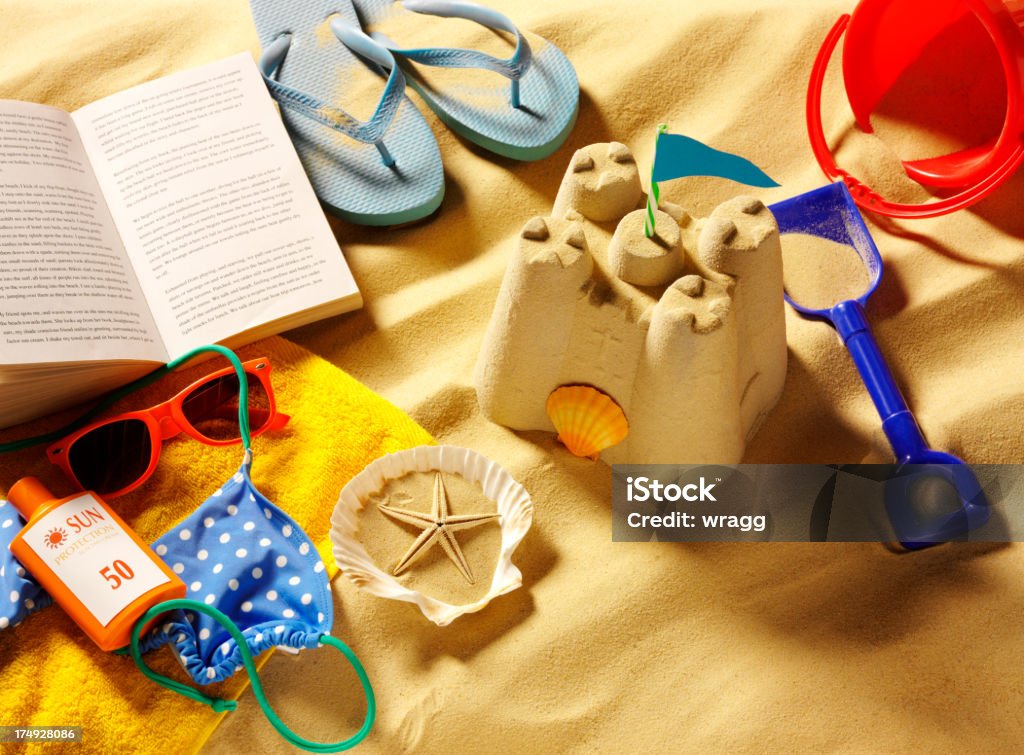 Castelo de areia na praia com um livro e chinelos - Foto de stock de Amarelo royalty-free