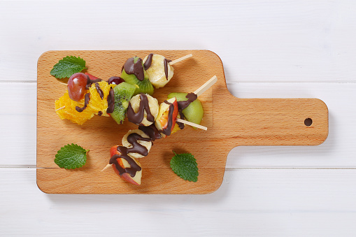 fruit kabobs with chocolate drizzle on wooden cutting board