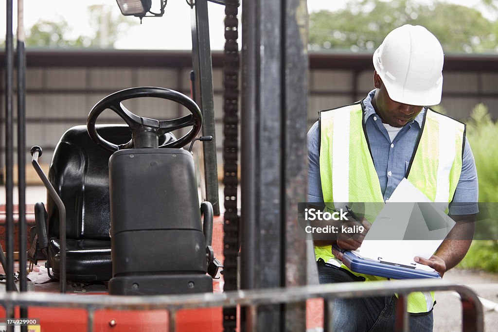 Trabalhador ao lado de empilhadeira escrevendo na área de transferência - Foto de stock de Empilhadeira royalty-free