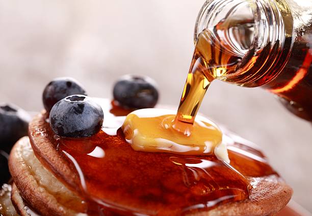 Pouring syrup Close-up of pouring maple syrup on stack of pancakes. maple syrup stock pictures, royalty-free photos & images