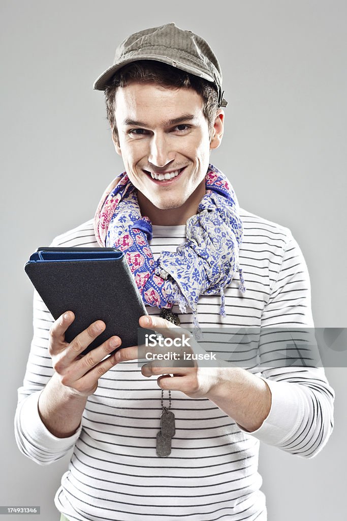 Young man using e-reader Young adult male tourist reading a guidebook using e-reader, smiling at the camera. Studio shot, grey backgroound. 20-24 Years Stock Photo