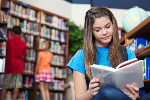 Middle school age girl reading book in school library.