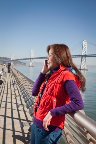 An Asian women talks on the phone beneath the San Francisco Bay Bridge.
