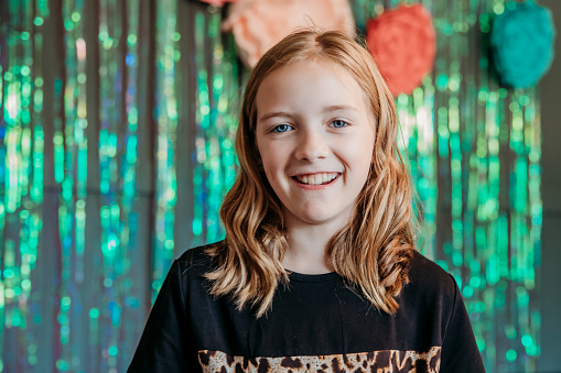 An elementary-aged girl poses in front of a shimmery backdrop and smiles at the camera