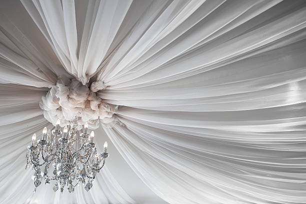 Festive ceiling decoration for weddings or ballroom with a crystal chandelier and white lacy fabric spreading out in soft waves