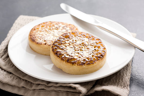 Two cooked crumpets with butter served up on a plate
