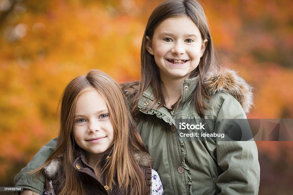 Due piccole sorelle in piedi fuori in fresca giornata autunnale - Foto stock royalty-free di Abbracciare una persona
