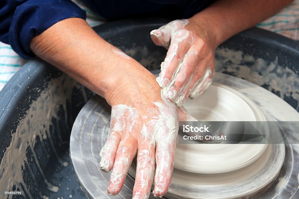 Pottery studio A lady ceramics artist at work in her home pottery studio, throwing a bowl on a wheel. Opening up. Adult Stock Photo