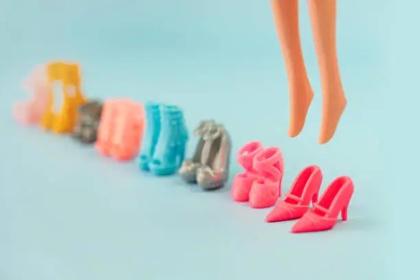 Plastic doll legs in toy shoes and a lot of different stylish fashionable shoes on a pink background. educational games for children. changing shoes games. put on shoes