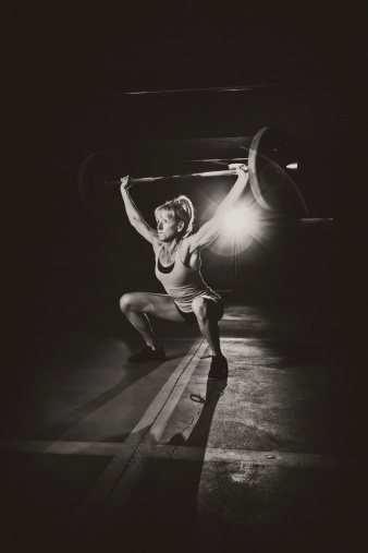 Very strong adult woman lifting weights, frontal view. Black and white with light flare