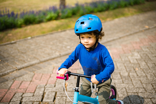 boy with sports helmets driving balance bike outdoors on a sunny day. He is learning new skill.