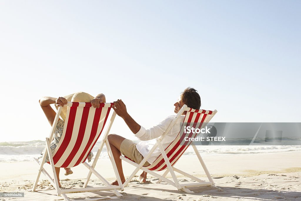 This is the life A happy couple sitting in deck chairs on the beach together - Copyspace Beach Stock Photo
