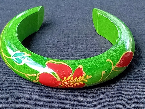 Green teak bracelet with red hibiscus flower pattern placed on a black background. Close -up shot of the bracelet.