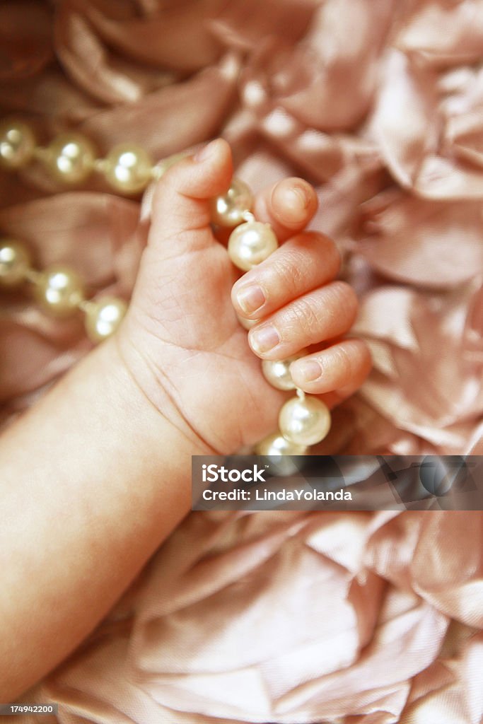 Newborn Baby's Hand Gripping Pearls A close up of a newborn baby's hand gripping a string of pearls. Pink satin background. 0-1 Months Stock Photo
