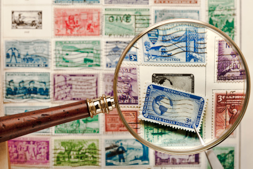 Moscow, Russia, March 2022: Hobby: stamp collecting. Looking at blurred old stamps through a golden magnifying glass. Copy space.