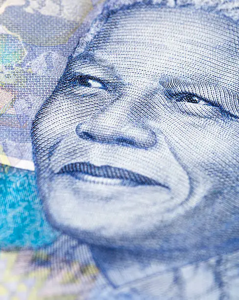 "Extreme close-up of a detail of a new South African Hundred Rand banknote, featuring an engraving of the face of iconic statesman Nelson Mandela, giving his trademark smile. South African wildlife and African designs form the watermarked background."