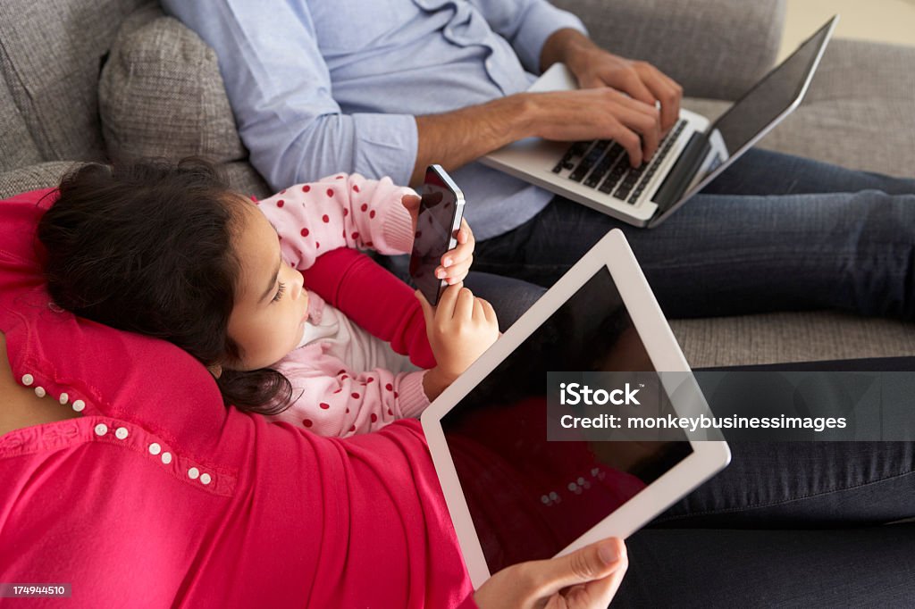 Family on sofa together with smartphone, laptop, and tablet Family On Sofa Using Smartphone, Laptop And Digital Tablet 30-39 Years Stock Photo