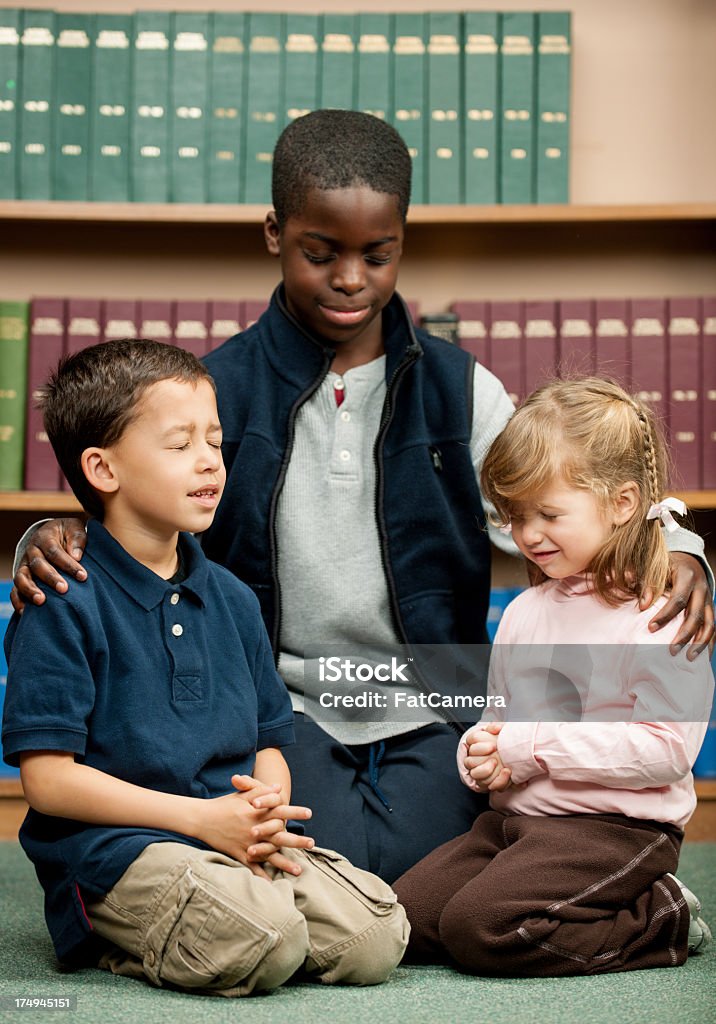 Praying Children praying together in a library. African Ethnicity Stock Photo