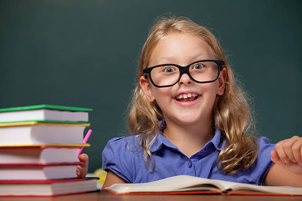 istock Smiling little school girl thinking on desk before blackboard 174947593