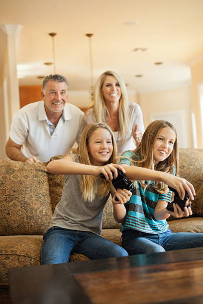 Happy sisters playing video game together Happy sisters playing video game together while parents standing behind sofa at home teenager couple child blond hair stock pictures, royalty-free photos & images