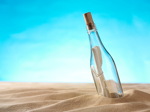 Copy space on a blue paper background with message in a bottle on a sandy beach.Click on the link below to see more of my travel images.