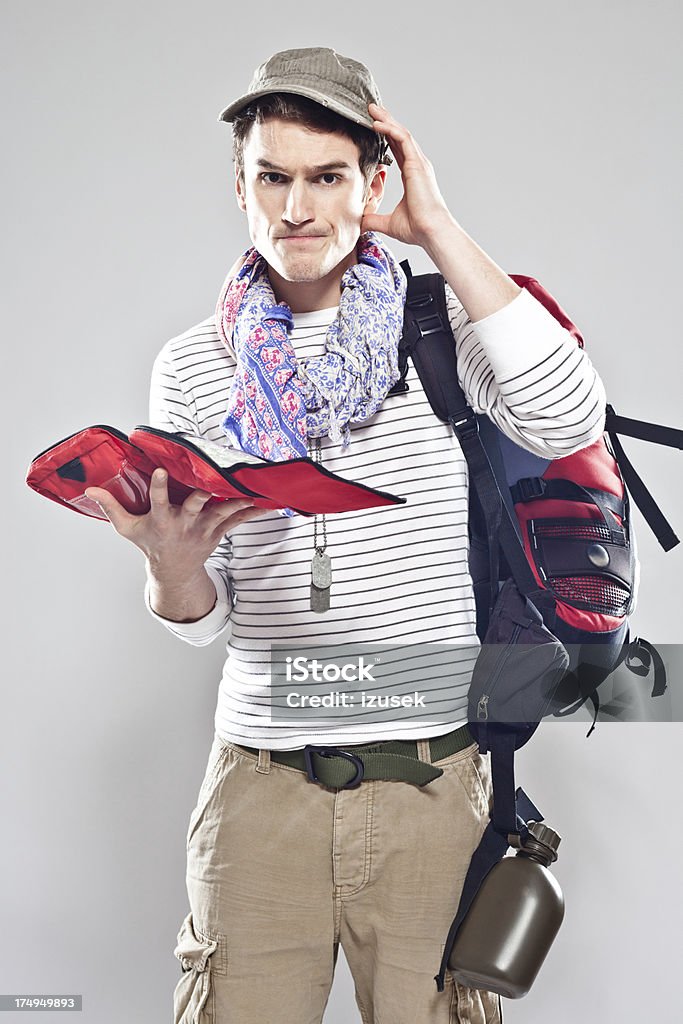 Tourist holding firts aid kit Young adult male backpacker holding a first aid kit in his hand and worried looking at the camera. Young Men Stock Photo