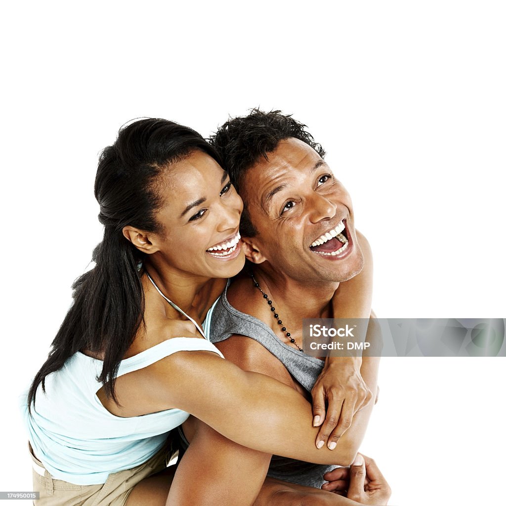 Smiling man piggybacking his girlfriend Portrait of happy young guy carrying his girlfriend on his back smiling and looking up against white background Couple - Relationship Stock Photo