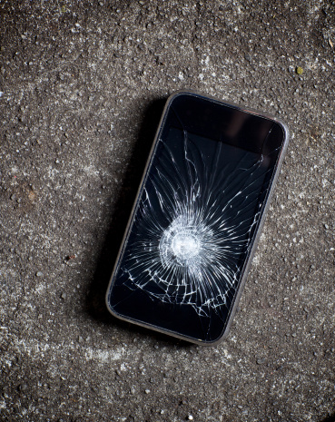 A smart phone with a broken screen sits atop a rough cement surface.