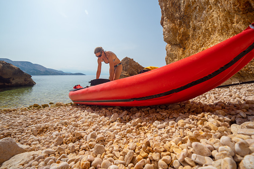 Low angle view sporty mature adult woman preparing her kayak on small stone beach on island of krk in croatia