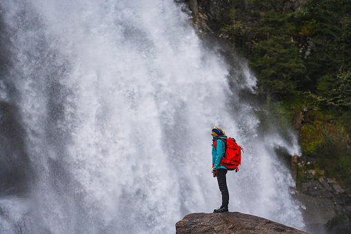 one mature adult sporty woman with huge backpack standing on rock near waterfall in austrian mountains