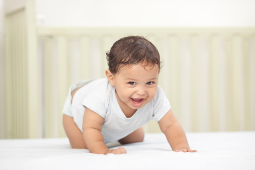 An adorable laughing baby looking at camera while he crawls on bed.