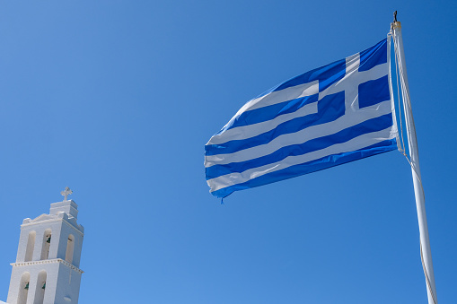 View of the national Greek flag and the top of a whitewashed Greek Orthodox Church in Ios Greece