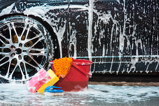 Cleaners and cleansers Bucket with sponges and brush with lots of foam next to car tire. bucket and sponge stock pictures, royalty-free photos & images