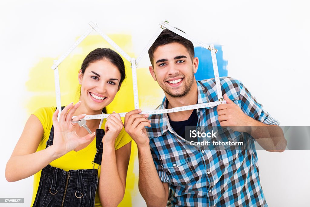 Couple holding a house shaped measure Home improvement series - Young couple holding a house shaped measure next to the painted wall, woman holding a key. Couple - Relationship Stock Photo