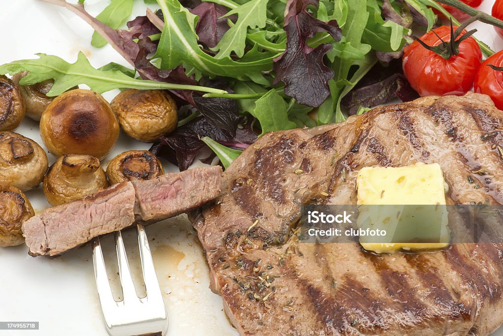 Grilled ribeye steak "Grilled ribeye steak served with salad leaves, mushrooms and grilled tomatoes on the vine - studio shot" Arugula Stock Photo
