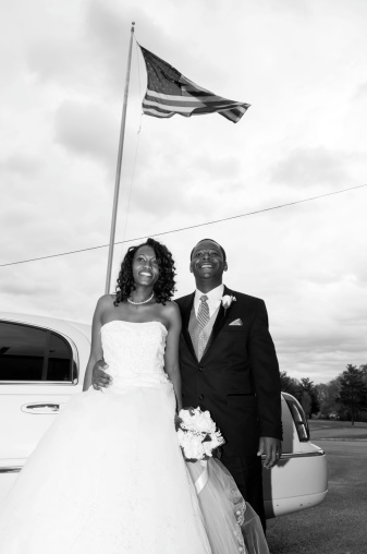 Black bride and groom couple standing outside their limo under the American flag
