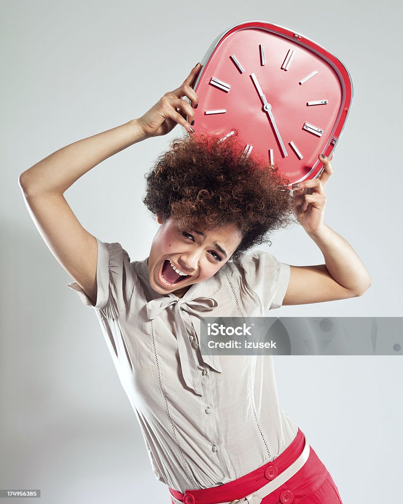 Gril with Red Clock Portrait of teenaged afro girl holding a big red clock above her head. Studio shot, grey background. Bad News Stock Photo