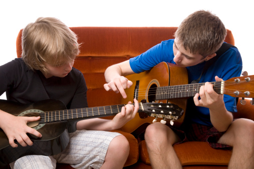 A teenage boy teaching an eight year old boy to play guitar. Positive relationships concept.Isolated on white.