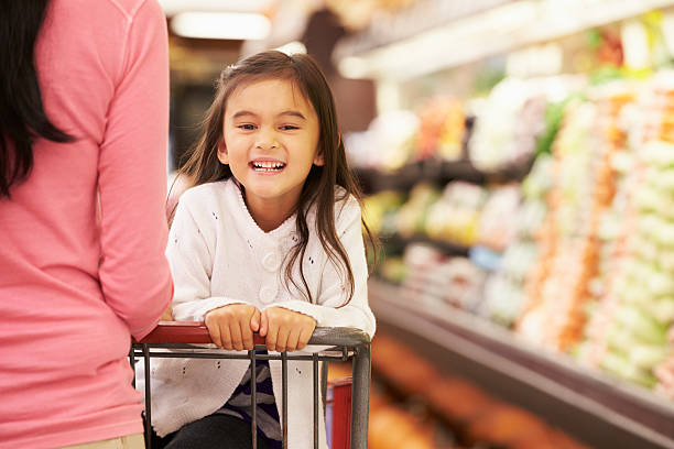 Close-up of mother pushing happy daughter in a store cart Close Up Of Mother Pushing Daughter In Supermarket Trolley Smiling To Camera supermarket family retail cable car stock pictures, royalty-free photos & images