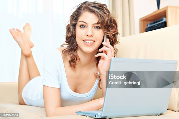 Young Woman Using Laptop While Speaking On Cellphone Stock Photo - Download Image Now