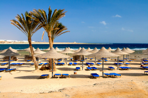 Blue sunbeds and straw umbrellas at exotic beach in Egipt.