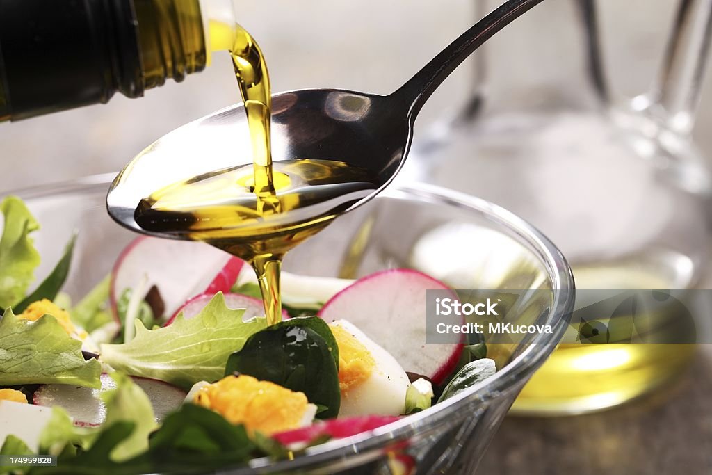 Adding dressing to a salad in a glass bowl Vegetable salad with eggs and pouring oil. Olive Oil Stock Photo