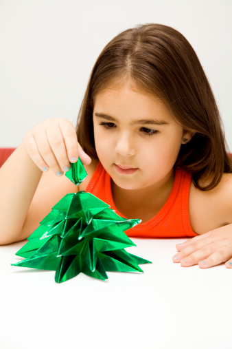 Girl making an origami christmas tree.See more images related with childhood