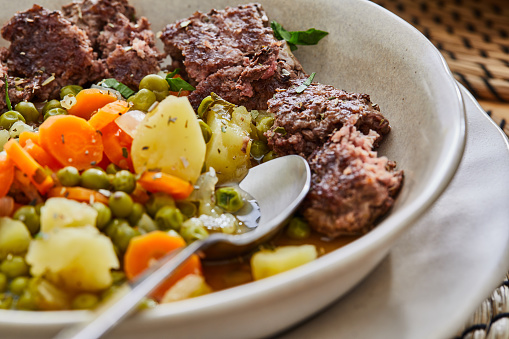 Green peas and beef meat, a healthy protein lunch after the workout, made of beef meat, green peas, potatoes, carrot and garlic, served in a modern plate on a rustic wooden home or restaurant table, representing a wellbeing and a healthy lifestyle, an image with a copy space