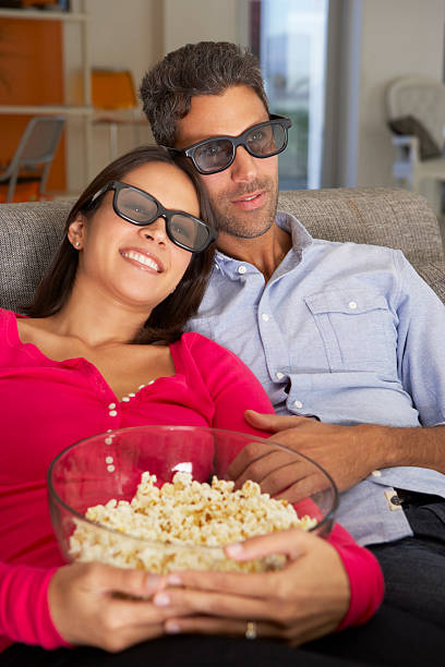 istock Couple On Sofa Watching TV Wearing 3D Glasses Eating Popcorn 174961008